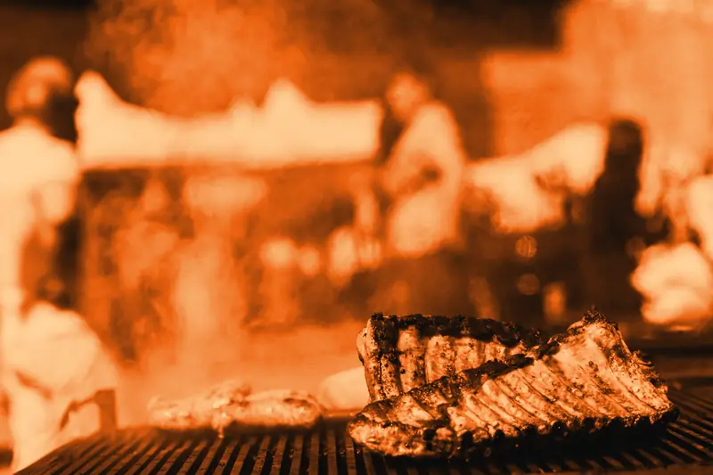 Travers de porc et saucisses qui grillent sur un barbecue fumant, visiteurs et tentes de stands flous en arrière-plan