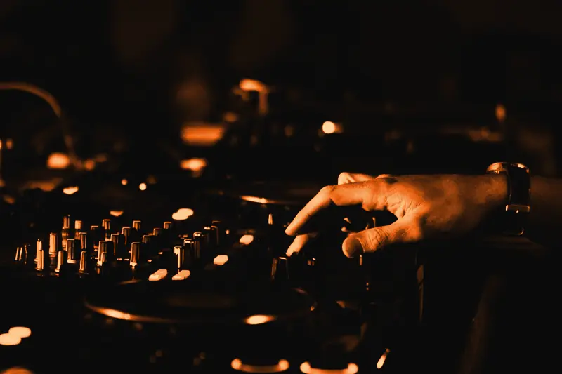 Main d'un DJ réglant les potentiomètres d'une table de mixage aux touches lumineuses
